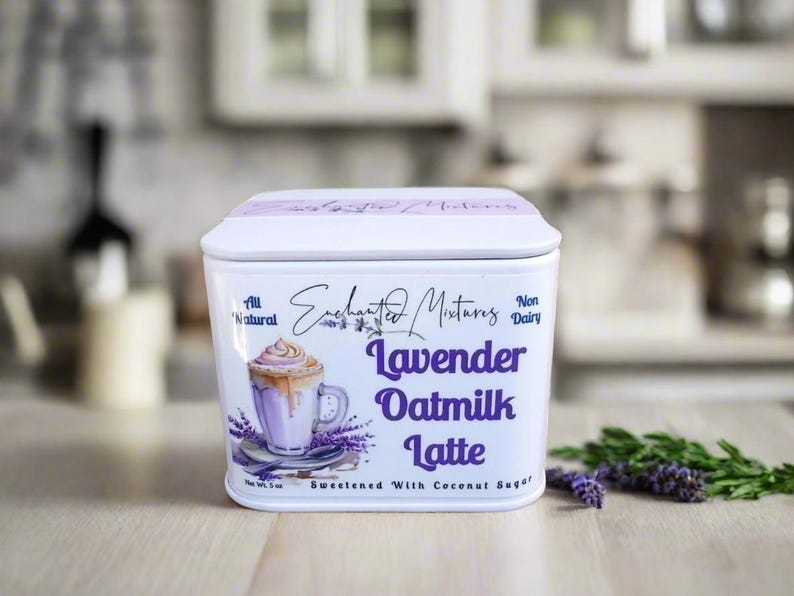 K&ouml;nnte beinhalten: Wei&szlig;e Blechdose mit einer Illustration von einem Lavendel-Hafermilch-Latte. Der Text auf der Dose lautet "Enchanted Mixtures, All Natural, Non Dairy, Lavender Oatmilk Latte, Sweetened with Coconut Sugar".