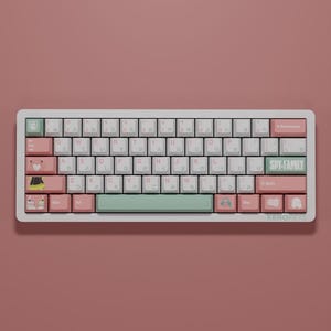 Può includere: Una tastiera meccanica personalizzata con tasti bianchi, rosa e verdi. La tastiera presenta caratteri giapponesi e il testo "SPY-FAMILY". I tasti hanno varie illustrazioni e il marchio "KENOREYS" è visibile.