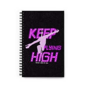 Könnte beinhalten: Schwarzer Spiralblock mit einer pinkfarbenen Silhouette einer Frau an einer Stange mit dem Text "KEEP FLYING HIGH" in pinkfarbenen umrandeten Buchstaben mit weißen Glühbirnen. Der Text "WICKED SIDE OF YOU" befindet sich unterhalb der Silhouette.
