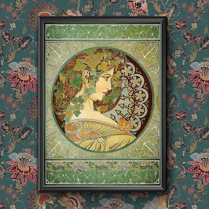 Op de afbeelding: Een vintage art nouveau-stijl illustratie van een vrouw met los haar, omringd door groene klimopbladeren en bloemen. De vrouw draagt een vloeiende jurk en heeft een delicaat bloemenpatroon op haar jurk. Het kunstwerk is ingelijst in een zwart frame.