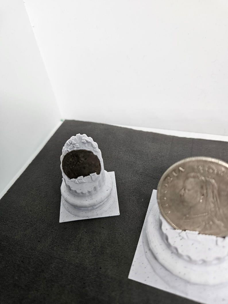 May include: Two small, white, decorative columns with a coin on top of one. The columns have a detailed, textured design. The coin features a profile of a person. The background is a dark gray surface.