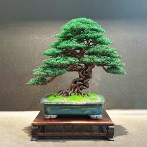 May include: A wire bonsai tree sculpture featuring a twisted dark brown trunk and branches with vibrant green foliage. The tree is planted in a rectangular teal ceramic pot with a mossy surface, resting on a dark wooden display stand.