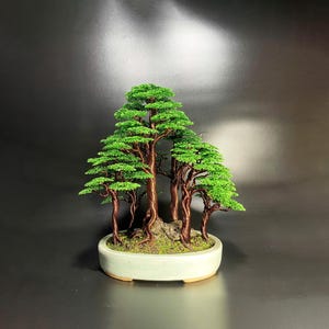 May include: A handcrafted bonsai tree sculpture. The miniature trees feature green foliage and copper-colored trunks, set in a light green ceramic pot. The bonsai arrangement is a decorative piece, perfect for home decor.