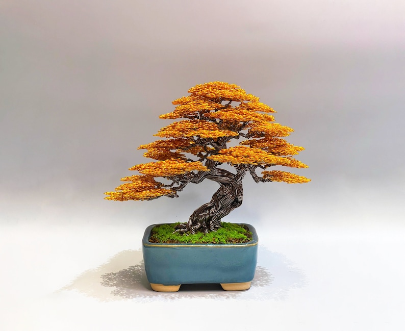 Puede incluir: Una escultura de alambre de un &aacute;rbol bons&aacute;i con hojas naranjas en una maceta de cer&aacute;mica azul. El &aacute;rbol est&aacute; hecho de alambre y cuentas, y la maceta est&aacute; esmaltada.