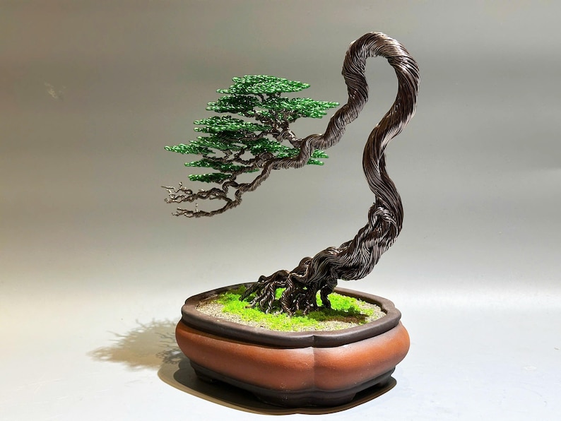 May include: A wire sculpture of a bonsai tree with green leaves and a brown pot. The tree is made of twisted wire and has a realistic appearance.