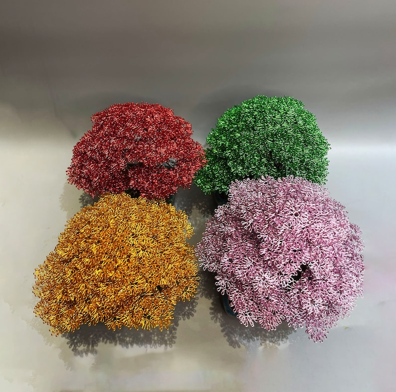 Puede incluir: Cuatro &aacute;rboles bonsai de alambre en diferentes colores: rojo, dorado, rosa y verde. Los &aacute;rboles est&aacute;n hechos de alambre y est&aacute;n dispuestos en un cuadrado.