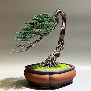 May include: A wire sculpture of a bonsai tree with green leaves and a brown pot. The tree is made of twisted wire and the leaves are made of small green beads.