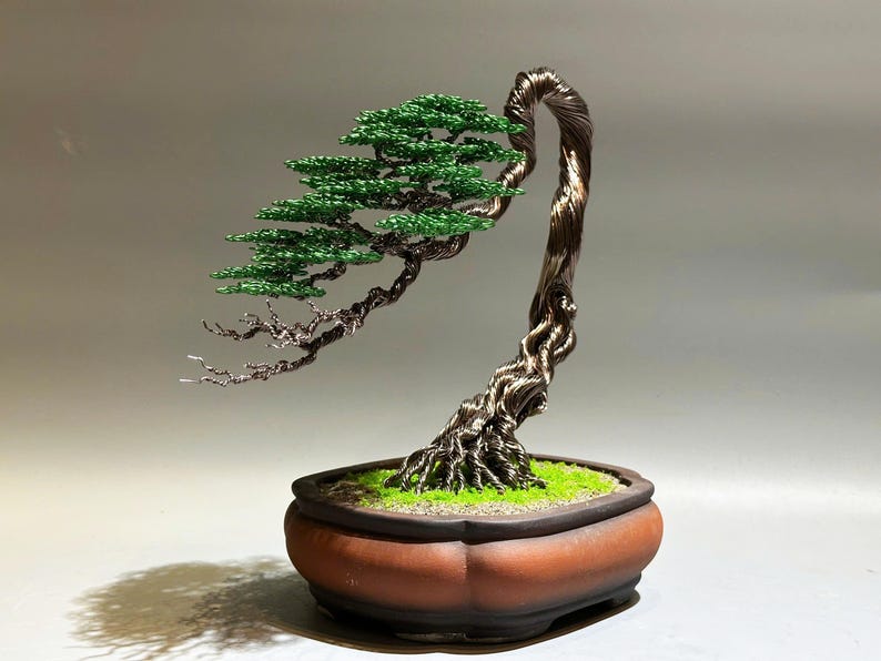 May include: A wire sculpture of a bonsai tree with green leaves and a brown pot. The tree is made of twisted wire and the leaves are made of small green beads.