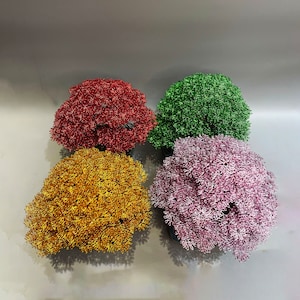 May include: Four wire bonsai trees in different colors: red, gold, pink, and green. The trees are made of wire and are arranged in a square.