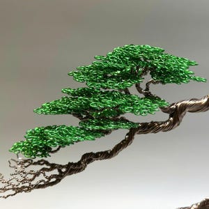 May include: A wire sculpture of a bonsai tree with a twisted trunk and green leaves. The tree is made of copper wire and green beads.