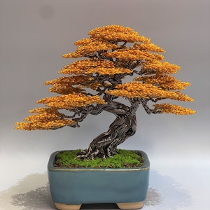 Puede incluir: Una escultura de alambre de un &aacute;rbol bons&aacute;i con un tronco marr&oacute;n y hojas naranjas. El &aacute;rbol est&aacute; en una maceta de cer&aacute;mica azul con una base de musgo verde.