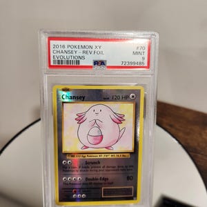 May include: A graded Pokémon card featuring Chansey from the 2016 XY Evolutions set. The card is encased in a clear protective holder and has a mint condition grade of 9. The card's artwork depicts a pink Chansey with a white belly.