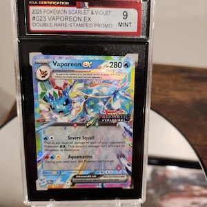 May include: A graded Pokémon card featuring Vaporeon EX from the Scarlet & Violet series. The card is encased in a protective holder and has a mint condition grade of 9. The card has a holographic design with blue and white colours.