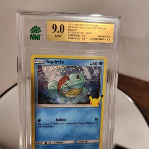 May include: A graded Pokémon trading card featuring Squirtle, a blue turtle-like creature. The card is from the McDonald's 25th Anniversary set and is graded 9.0 by MNT. The card's details include the text "Bubble" and "HP 60".