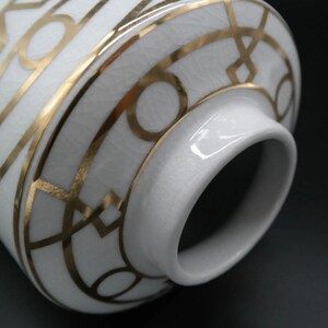 Pode incluir: Vaso de cer&acirc;mica branca com um design geom&eacute;trico dourado. O vaso tem uma abertura larga e um fundo arredondado.