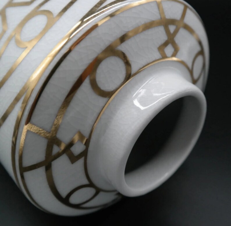 Pode incluir: Vaso de cer&acirc;mica branca com um design geom&eacute;trico dourado. O vaso tem uma abertura larga e um fundo arredondado.