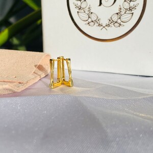 May include: Gold-toned ear cuff with a twisted, geometric design. The cuff is made of metal and has a simple, modern style.