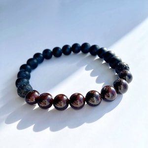 Op de afbeelding: Een armband met afwisselend matte zwarte en dieprode kralen. De zwarte kralen hebben een matte afwerking, terwijl de rode kralen gepolijst en glanzend zijn. De armband bestaat uit ronde kralen die op een elastische band zijn geregen.