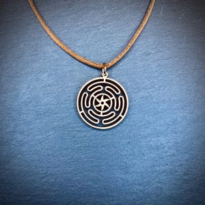 May include: A wooden pendant necklace with a brown leather cord. The pendant is a circular design with a five-pointed star in the center and concentric circles radiating outward.