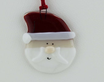 May include: A glass ornament shaped like Santa Claus's face. The ornament is white with a red hat and a white beard. The ornament has a black string for hanging.