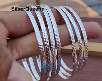 Pode incluir: Conjunto de cinco pulseiras de prata martelada. As pulseiras estão empilhadas umas sobre as outras e têm um acabamento martelado texturizado.