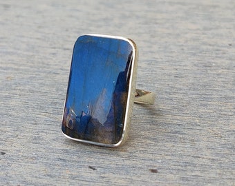 Può includere: Un anello d'argento con una pietra rettangolare di labradorite blu. La pietra ha un effetto iridescente scintillante.