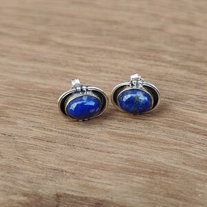 Könnte beinhalten: Ein Paar silberne Ohrringe mit ovalen Lapislazuli-Steinen. Die Steine sind tiefblau mit weißen Flecken.