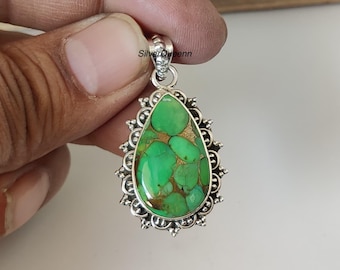 May include: A silver pendant with a teardrop-shaped, green and gold stone. The stone is surrounded by a decorative silver frame with a detailed design. The pendant has a loop at the top for a chain. The text "SilverQueenn" is visible.