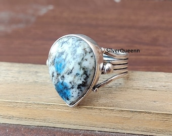 May include: A silver ring with a teardrop-shaped blue and white gemstone. The ring has a twisted band with a beaded detail.