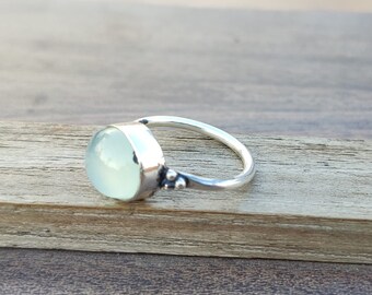 May include: A silver ring with a light blue oval gemstone. The ring has a simple design with a smooth band and a small detail on the side.