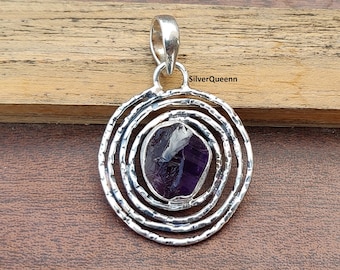 May include: A silver pendant with a purple amethyst stone set in a circular design with concentric circles.