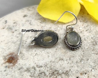 May include: A pair of silver earrings with a green gemstone set in a silver bezel. The earrings have a simple, elegant design and are perfect for everyday wear.