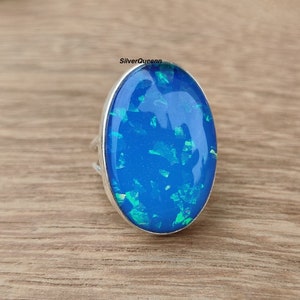 May include: A silver ring featuring a large oval blue opal gemstone. The opal displays a shimmering green and blue iridescent effect.
