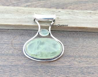 May include: A silver pendant with a green aventurine gemstone and a smaller clear gemstone. The pendant is oval shaped and has a bail for attaching to a chain.