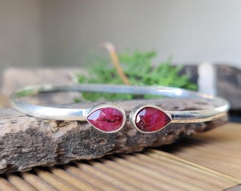 Puede incluir: Una pulsera de plata con dos gemas rojas en forma de lágrima. La pulsera tiene un diseño sencillo y elegante, ideal para el uso diario. Las gemas están engastadas en una montura de plata pulida.