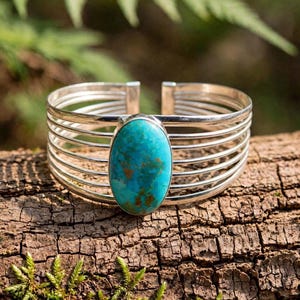 May include: A silver cuff bracelet featuring a large, oval-shaped turquoise stone with brown matrix patterns. The band is constructed from five parallel silver wires that curve to form an open-ended circular shape around the wrist.