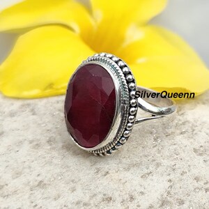 May include: A silver ring featuring a large, oval-shaped, red gemstone set in a beaded bezel. The ring has a simple band with a split shank.
