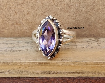 May include: A silver ring with a marquise-shaped amethyst gemstone. The ring has a beaded band and a delicate design.