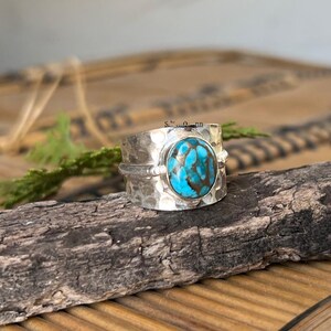May include: A silver ring with a hammered texture and a large, oval turquoise stone with brown matrix. The ring has a wide band and a simple design. The ring is suitable for everyday wear.