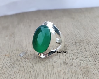May include: A silver ring with a green oval gemstone set in a unique, open design. The ring is on a wooden surface. SilverQueenn is written on the band.