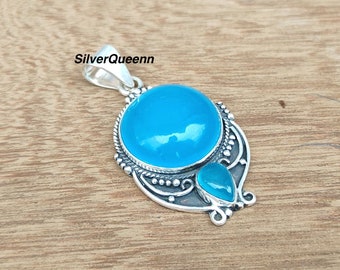 May include: A silver pendant with a large round blue gemstone and a smaller teardrop-shaped blue gemstone. The pendant has an intricate design with swirls and beads.