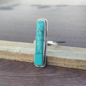 May include: A silver ring with a turquoise stone set in a rectangular shape. The stone has a marbled pattern and is a vibrant blue-green color.