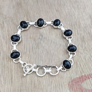 May include: A silver bracelet with black oval gemstones and a toggle clasp. The bracelet is made of sterling silver and features a simple design.