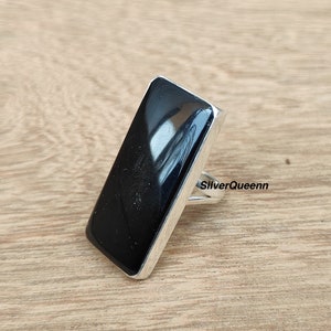 Könnte beinhalten: Ein silberner Ring mit einem schwarzen rechteckigen Stein. Der Ring liegt auf einer Holzoberfläche. Der Text "SilverQueenn" ist auf dem Ring sichtbar.