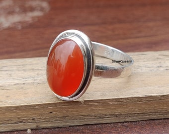 May include: A silver ring with an oval-shaped carnelian gemstone. The ring has a polished silver band and a double-lined border around the gemstone. The text "SilverQueenn" is engraved on the band.
