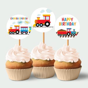 Op de afbeelding: Drie cupcakes versierd met rode, gele en blauwe cupcake-toppers met een treinthema. De toppers zeggen "Happy Birthday" en "Chugga Chugga Two".