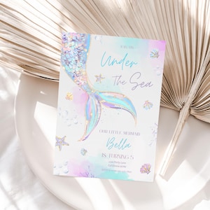 May include: A mermaid tail with iridescent scales and a gold glitter design on a light blue and pink watercolor background. The text "Join Us Under The Sea" is at the top of the invitation. The text "Our Little Mermaid Bella Is Turning 5" is at the bottom of the invitation. The invitation also includes the address and RSVP information.