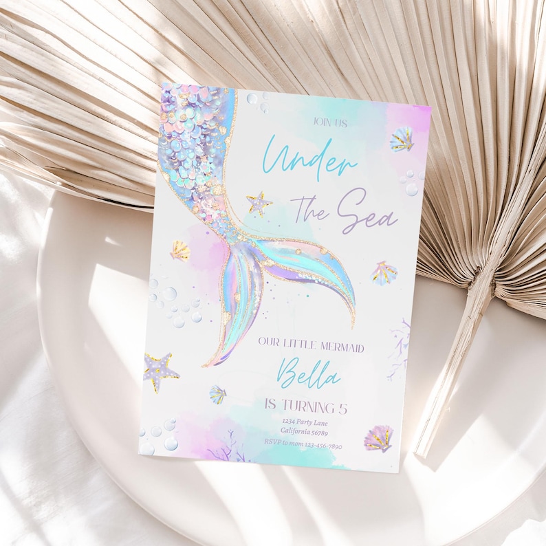 K&ouml;nnte beinhalten: Ein Meerjungfrauen-Schwanz mit schillernden Schuppen und einem goldenen Glitzer-Design auf einem hellblauen und rosafarbenen Aquarell-Hintergrund. Der Text "Join Us Under The Sea" befindet sich oben auf der Einladung. Der Text "Our Little Mermaid Bella Is Turning 5" befindet sich unten auf der Einladung. Die Einladung enth&auml;lt auch die Adresse und die RSVP-Informationen.