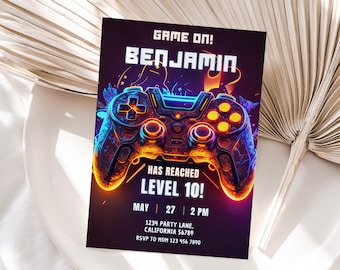 May include: A purple and orange video game controller with neon lights. The text "GAME ON! BENJAMIN HAS REACHED LEVEL 10! MAY 27 2 PM 1234 PARTY LANE, CALIFORNIA 56789 RSVP TO MOM 123 456 7890" is on the invitation.