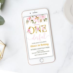 May include: A rose gold smartphone displays a first birthday invitation. The invitation features the words "little miss ONE derful" in gold and pink, with floral accents. The invitation includes the date, time, and location of the party.